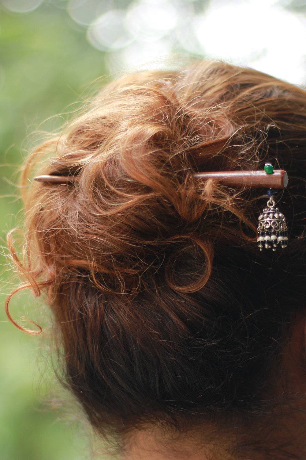 Close-up of a hairpin with decorative elements in a person's hair against a blurred natural background