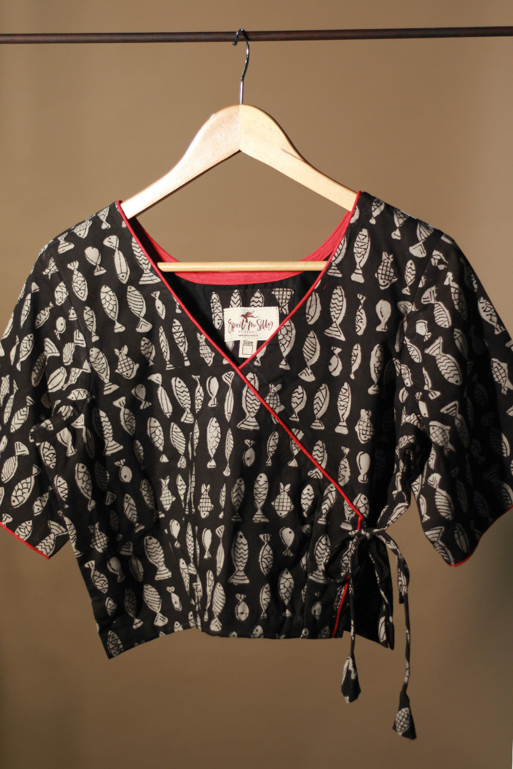 Black patterned top with red trim on a hanger against a brown background