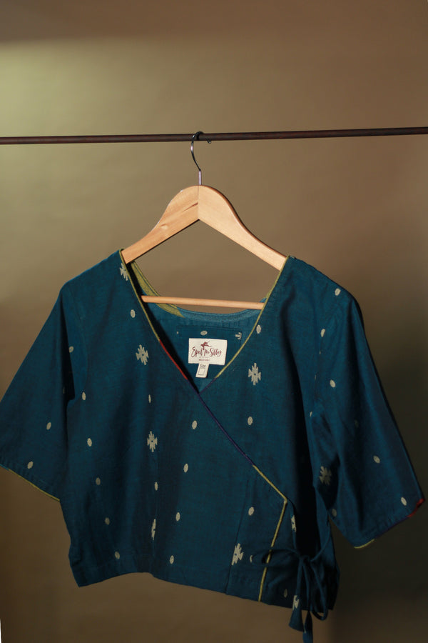 Blue top with white patterns on a wooden hanger against a beige wall
