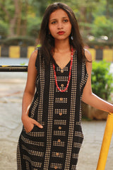 Woman in a black patterned dress with a red necklace outdoors.