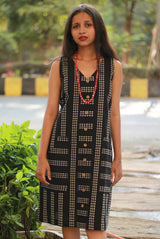 Woman wearing a black patterned dress outdoors with greenery in the background.