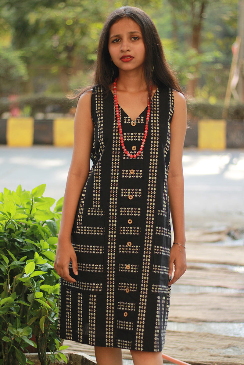 Woman wearing a black patterned dress outdoors with greenery in the background.