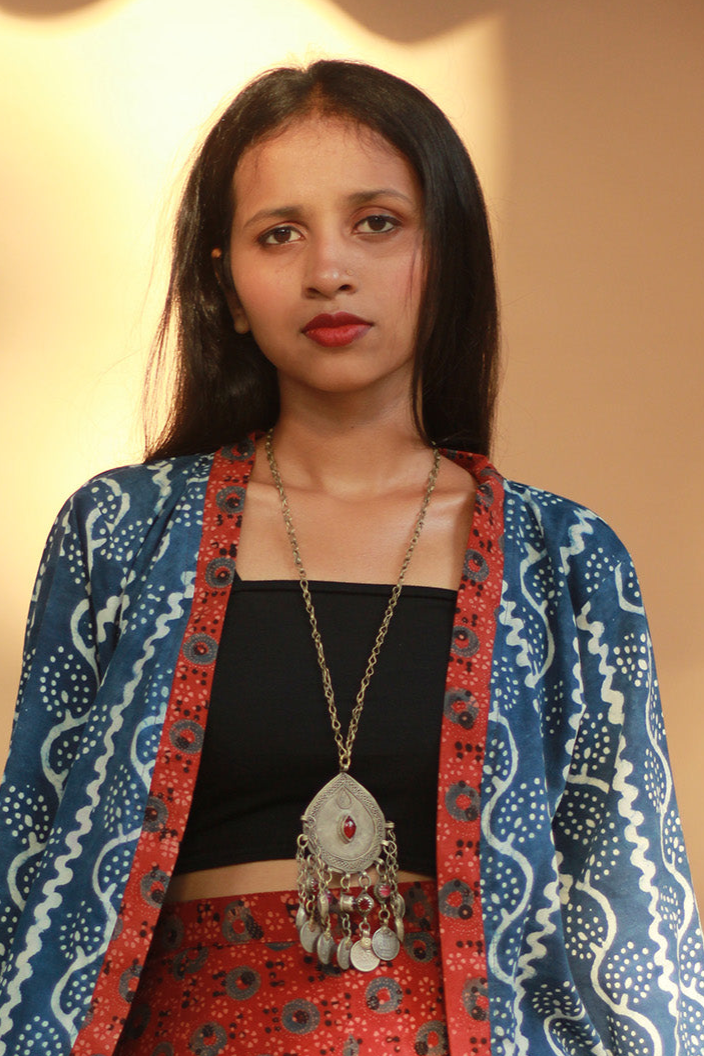 Woman wearing a blue patterned jacket with a red and black outfit underneath, against a plain background.