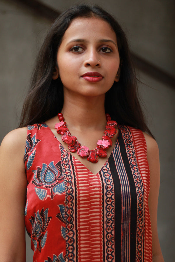 Woman wearing a red patterned dress with a matching necklace against a neutral background
