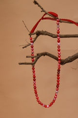 Red beaded necklace hanging on a branch against a brown background