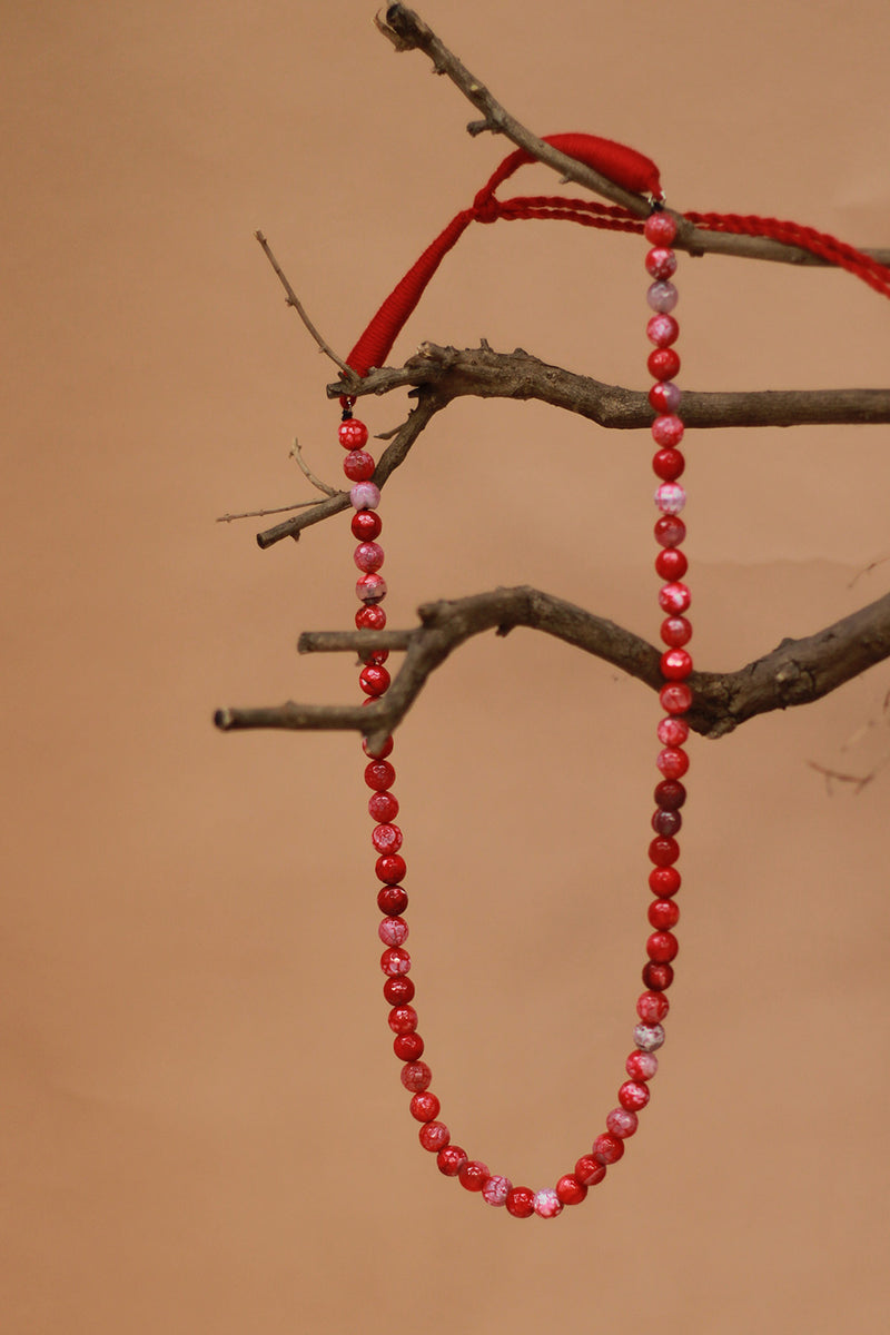 Red beaded necklace hanging on a branch against a brown background