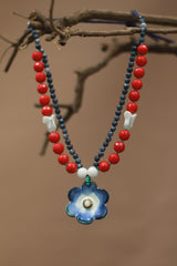 Necklace with red beads, blue flower pendant, and white accents on a brown background