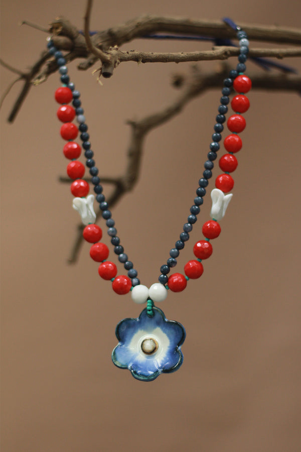 Necklace with red beads, blue flower pendant, and white accents on a brown background